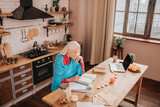 Grey-haired beautiful elderly lady in blue shawl sitting at the table