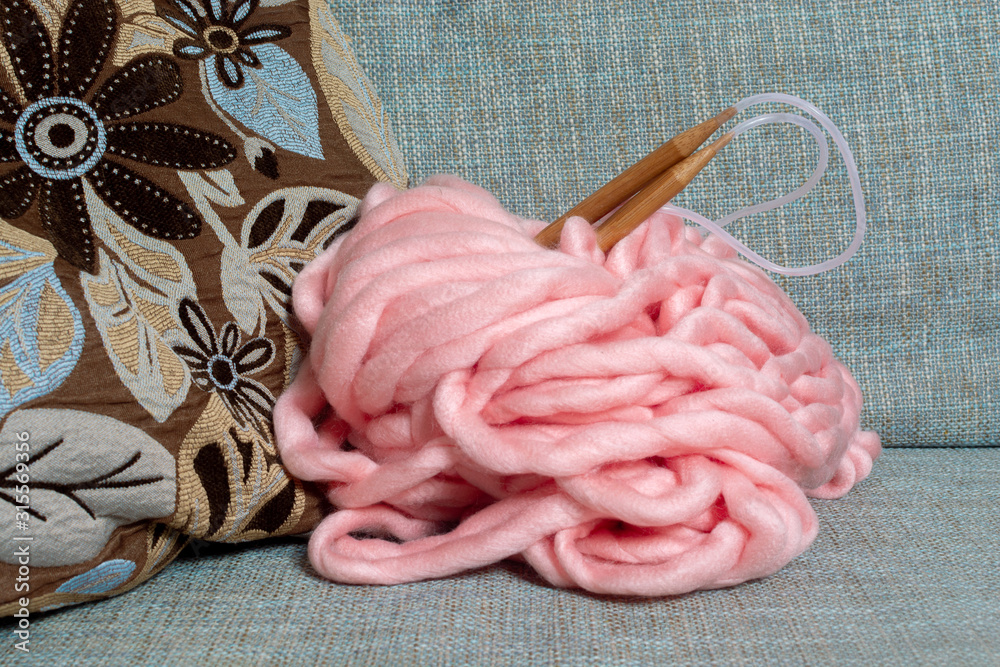 skein of giant merino pink yarn for arm knitting with large knitting needles  on a blue sofa Stock Photo