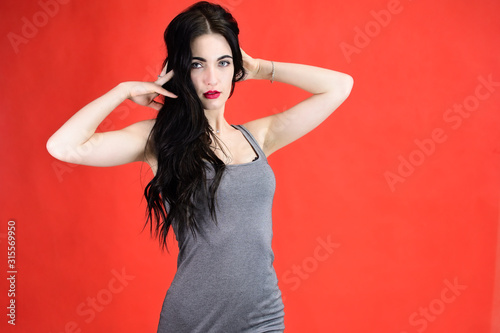 The concept of a beautiful female portrait with emotions. Portrait of a brunette girl with a smile with long hair with excellent makeup in a gray dress on a red background in different poses.