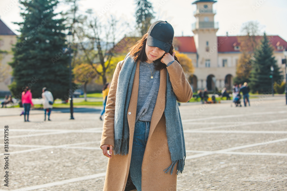 Fototapeta premium young pretty fashionable woman walking in brown coat by street
