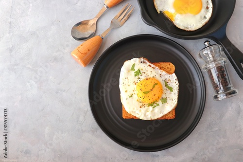 Fried Egg on Whole wheat Toast with salt and pepper for classic Breakfast. sunny side up egg with brown bread on black plate over wooden table, top view, copy space.