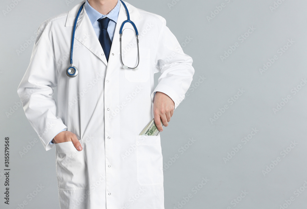 Doctor putting bribe money into pocket on grey background, closeup. Corruption in medicine Doctor putting bribe money into pocket on grey background, closeup. Corruption in medicine
