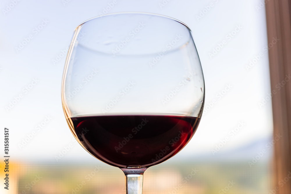 Closeup macro of one glass of dark red wine isolated in Italy Tuscany on windowsill window with blurry background view