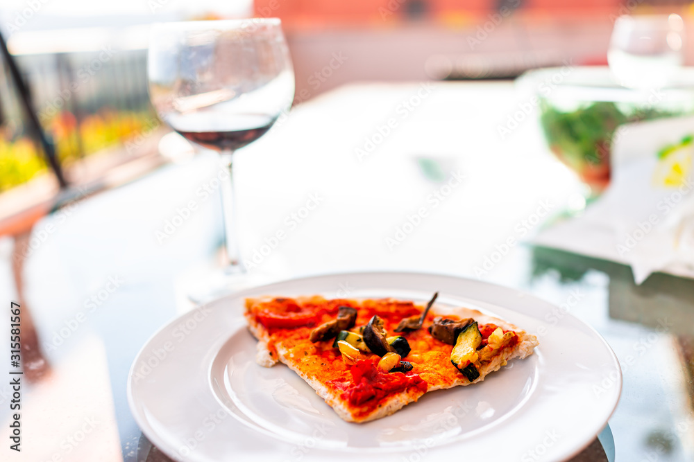 One pizza slice on white plate in Italy with vegan food tomato sauce chopped vegetables and red wine glass