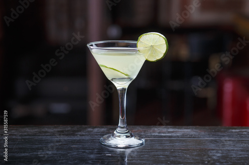 Cocktail with lime and rim, standing on the bar counter, isolated on a dark light background.