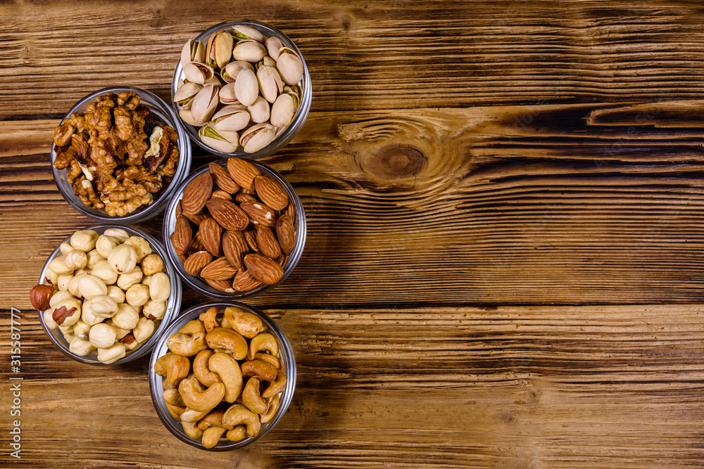 Various nuts (almond, cashew, hazelnut, pistachio, walnut) in glass bowls on a wooden table. Vegetarian meal. Healthy eating concept. Top view Various nuts (almond, cashew, hazelnut, pistachio, walnut) in glass bowls on a wooden table. Vegetarian meal. Healthy eating concept. Top view
