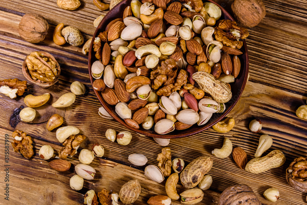 Various nuts (almond, cashew, hazelnut, pistachio, walnut) in ceramic plate on a wooden table. Vegetarian meal. Healthy eating concept. Top view