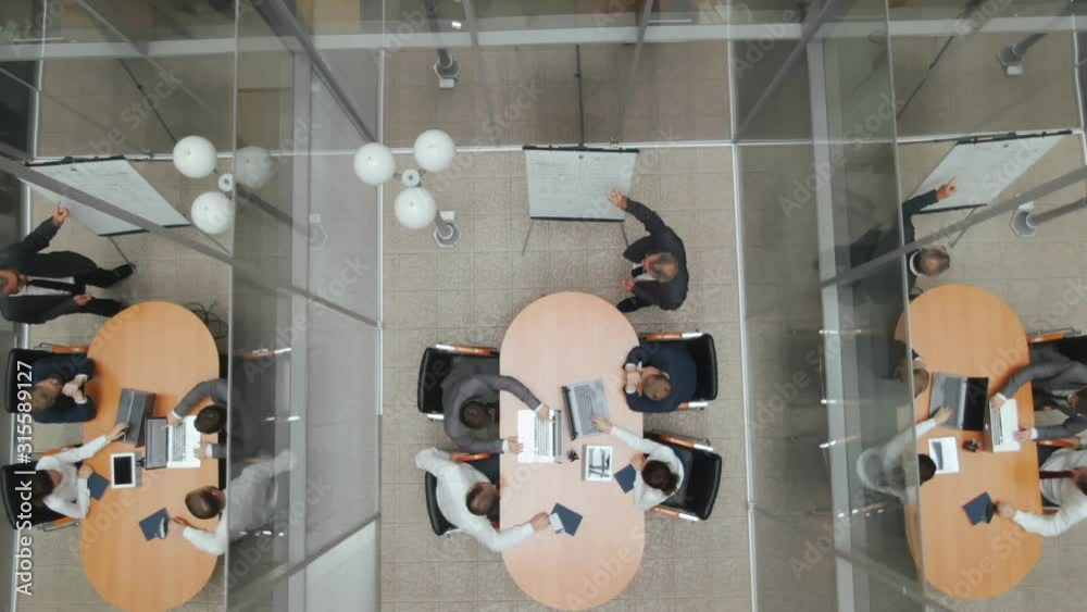 Top view corporate meeting room. Enthusiastic director makes presentation and delivers powerful speech to a board of executives. Senior boss talks about advantages of cooperation and communication