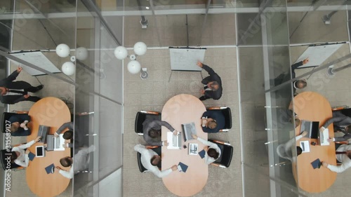 Top view corporate meeting room. Enthusiastic director makes presentation and delivers powerful speech to a board of executives. Senior boss talks about advantages of cooperation and communication