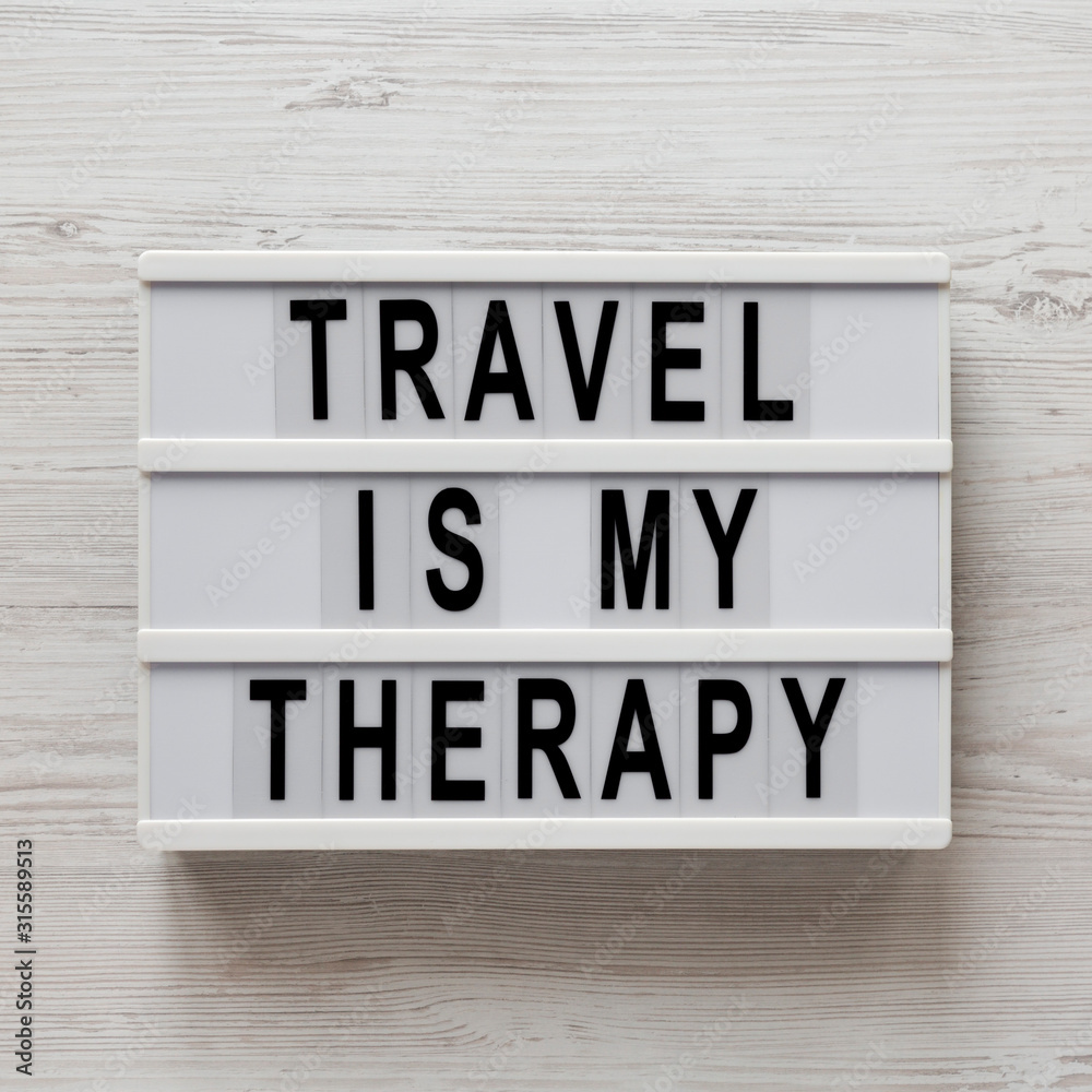 'Travel is my therapy' words on a modern board on a white wooden background, top view. Overhead, from above, flat lay. Close-up. 'Travel is my therapy' words on a modern board on a white wooden background, top view. Overhead, from above, flat lay. Close-up.