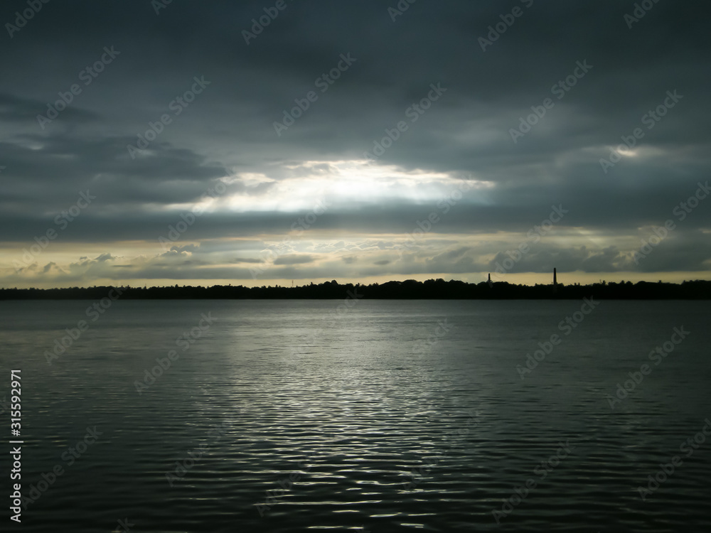 Beautiful Sun Rays of bright light shining through hole of dark clouds and illuminating lake water horizon in sunset time. Dramatic Texas sky atmosphere. Beauty in nature background. Beautiful Sun Rays of bright light shining through hole of dark clouds and illuminating lake water horizon in sunset time. Dramatic Texas sky atmosphere. Beauty in nature background.