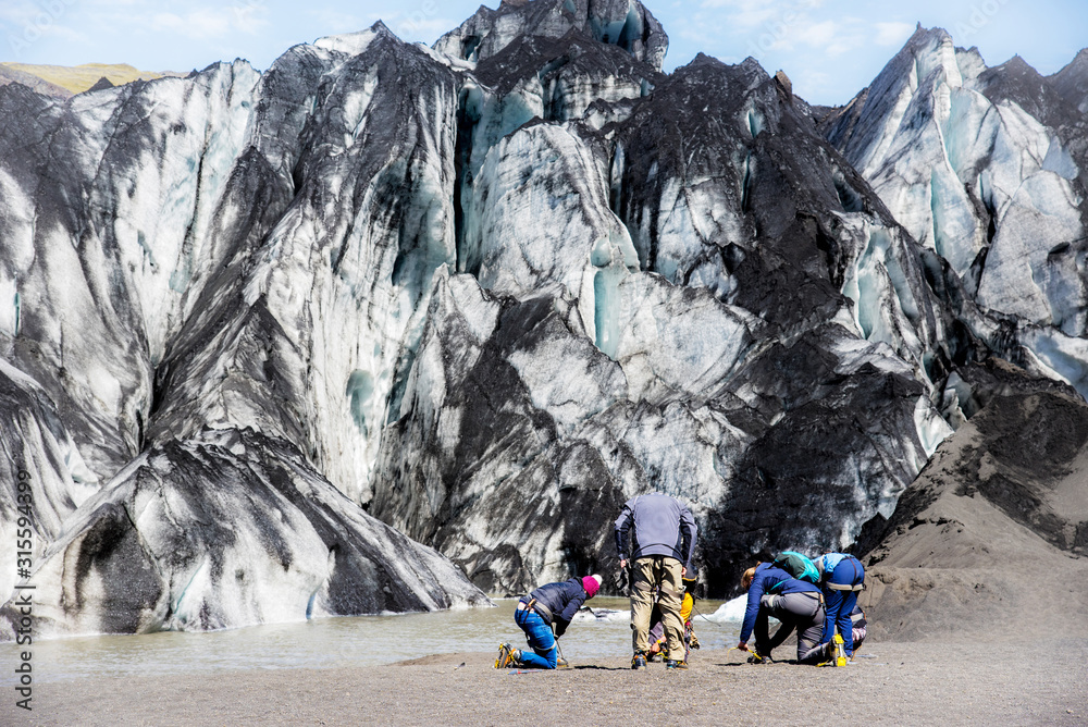 a group of tourists wears special shoes-claws for climbing on the glacier in volcanic soot in Solheimajokull lagune, Iceland. Exotic countries. Popular tourist atraction.