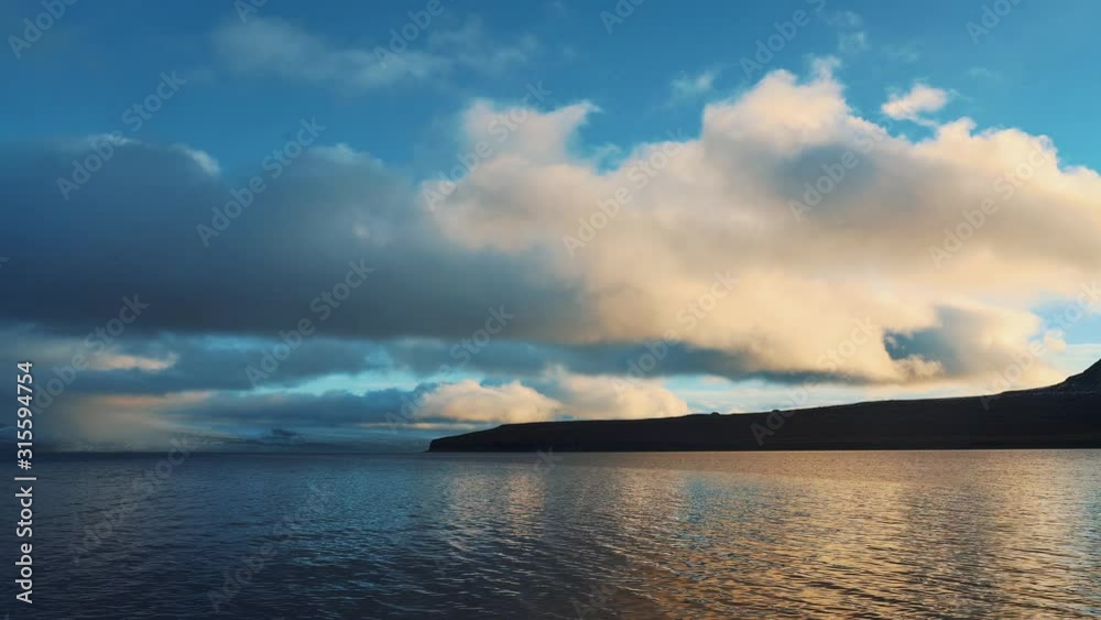 A Beautiful driving shot of arctic Peaceful Sea And Mountain Slope Under A Cloudy Blue Sky, Iceland, westfjords A Beautiful driving shot of arctic Peaceful Sea And Mountain Slope Under A Cloudy Blue Sky, Iceland, westfjords