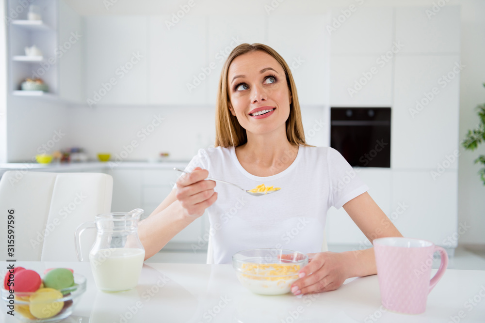 Photo of dreamer housewife holding spoon eating breakfast cornflakes healthy eating dieting looking dreamy up imagine herself chin sitting table white light kitchen indoors