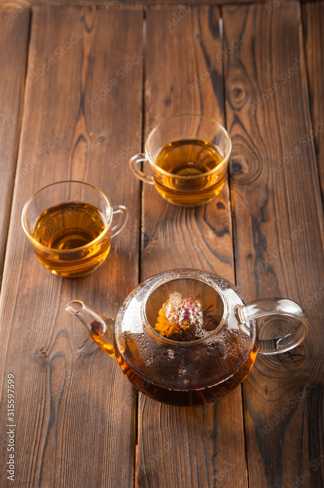 Knitted blooming tea in a transparent teapot close-up. Tea ceremony on a dark wooden background and copy space. Knitted blooming tea in a transparent teapot close-up. Tea ceremony on a dark wooden background and copy space.