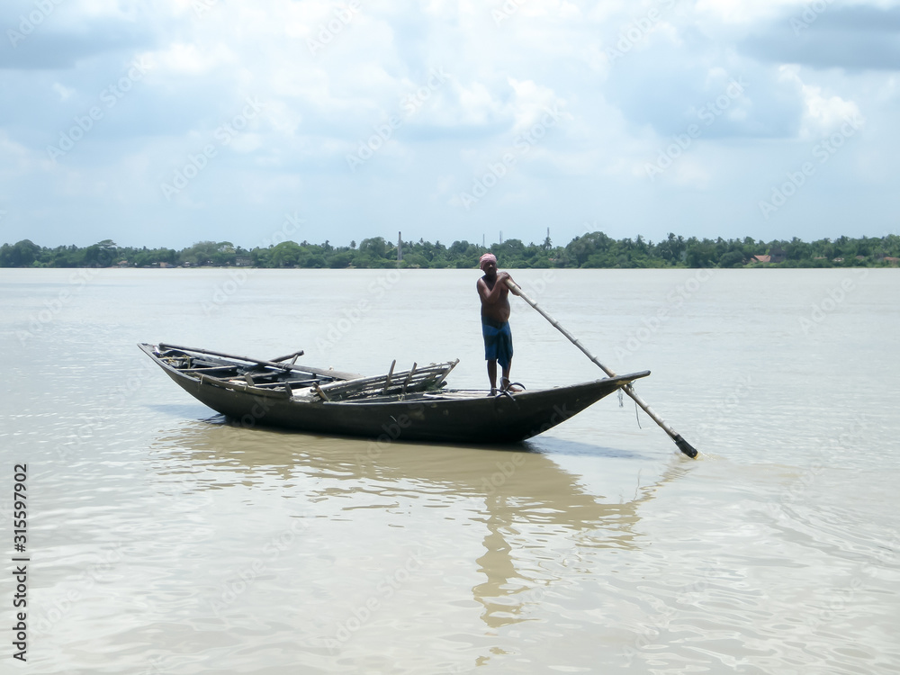 Traditional boatman (ferry people Majhi) rowing boat (called Nauka) on river Ganges (Ganga). Rural Indian travel tourism and water transportation theme. The Sundarbans West Bengal India South Asia Pac Traditional boatman (ferry people Majhi) rowing boat (called Nauka) on river Ganges (Ganga). Rural Indian travel tourism and water transportation theme. The Sundarbans West Bengal India South Asia Pac