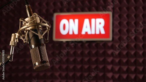 On Air sign lighting up in Broadcast TV Studio, Radio Station. There's a microphone in the foreground. Dolly Shot - Stock 4K Video Clip Footage photo