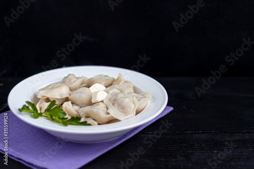 Boiled dumplings with feathers of green onions. In the background are greens, red peppers and bay leaves. On a black wooden background.