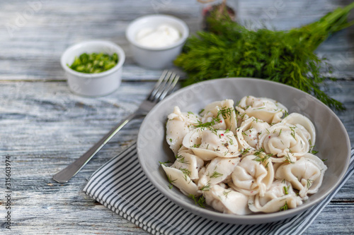 Boiled dumplings decorated with onions and peppers. In the background are greens, red peppers and bay leaves. On a light wooden background.