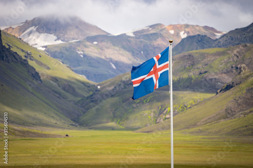 Flag of Iceland against the background of green mountains and blue sky