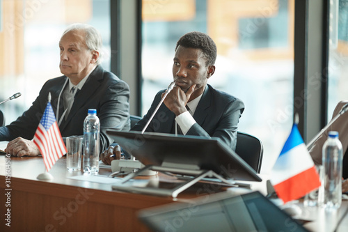 African young businessman and senior businessman sitting at the table and listening at conference