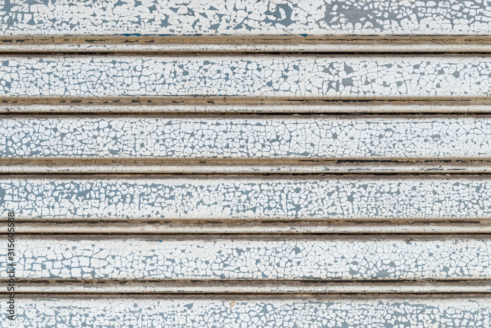Cracked white paint colors on stripe pattern of metallic roller shutter doors or rolling steel doors background. Cracked white paint colors on stripe pattern of metallic roller shutter doors or rolling steel doors background.