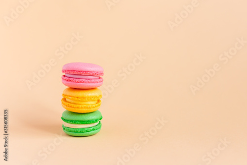 Three tasty french macarons on peach pastel background. Pink, yellow and green macarons.