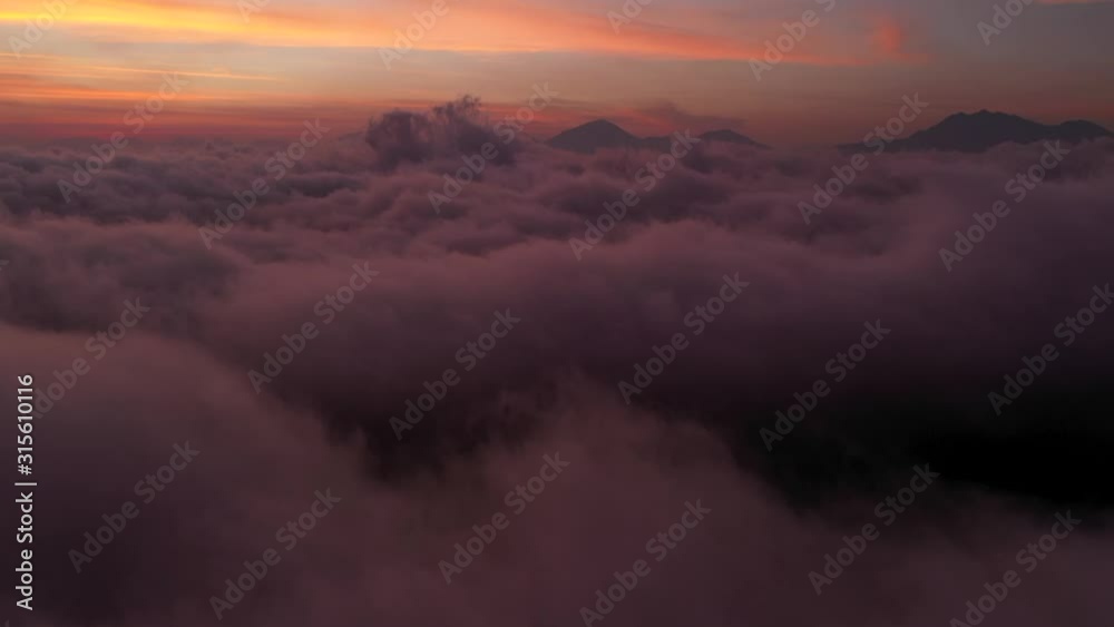 The beautiful fiery orange sunset beyond the clouds and mountain peaks of Bali, Indonesia - Aerial shot