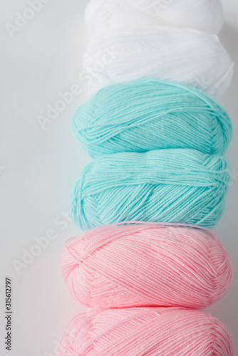 acrylic soft pastel pink, azure and white colored wool yarn thread skeins row on white background, top view flat lay vertical stock photo image mockup with copy space for text