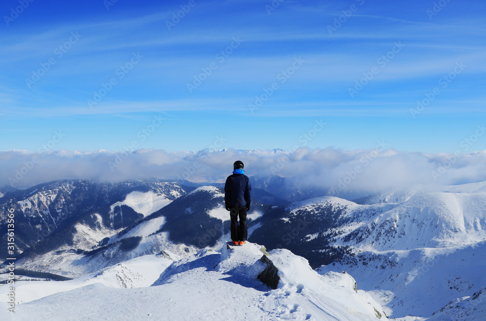 Young boy stands on peak of Chopok mountain and below it lies the Demanovska valley and in far High Tatras. Fairy-tale panorama with man in black clothes stands on the edge of mountain