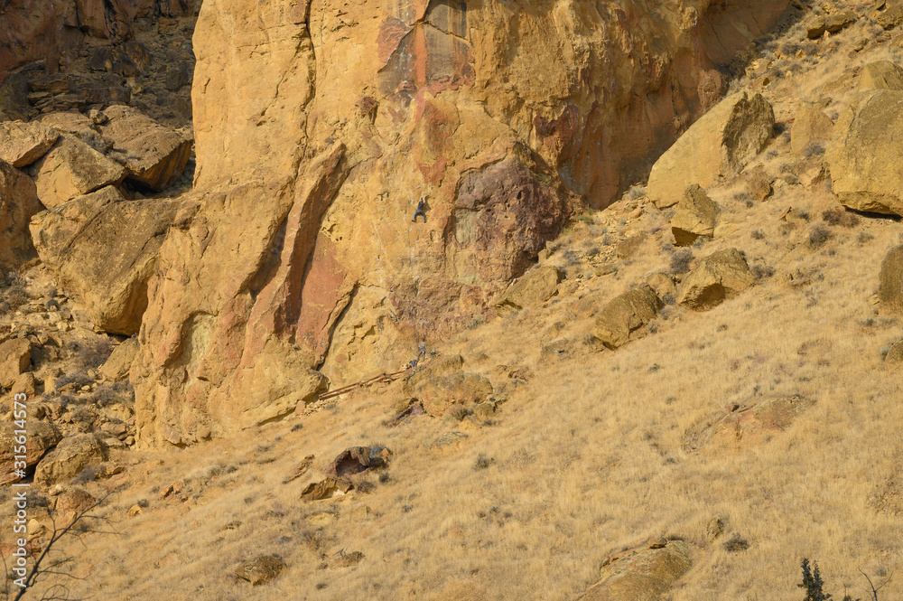 Rock climbers climb a large rock, filmed from the back.