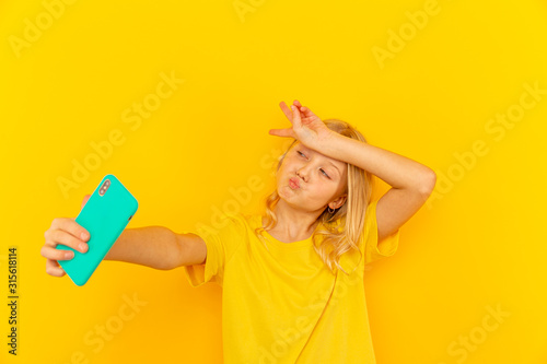 Smiling little girl kid showing blue screen of new popular mobile phone on light yellow background photo