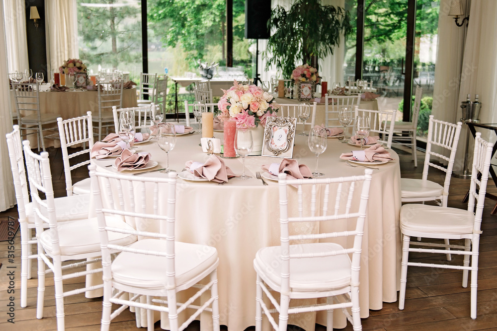 Wedding. Banquet. The chairs and round table for guests, served with cutlery, flowers and crockery and covered with a tablecloth Wedding. Banquet. The chairs and round table for guests, served with cutlery, flowers and crockery and covered with a tablecloth