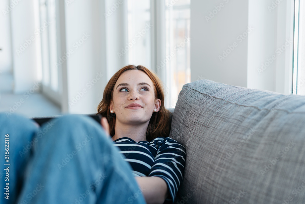 Young woman reclining on a couch daydreaming Young woman reclining on a couch daydreaming