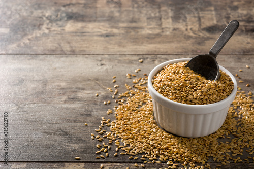 Golden flax seeds in white bowl on wooden table. Copy space