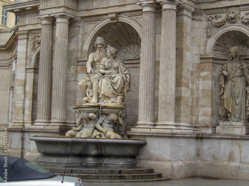 Marble sculpture with a fountain on the background of an old building with columns, stucco and stone carvings