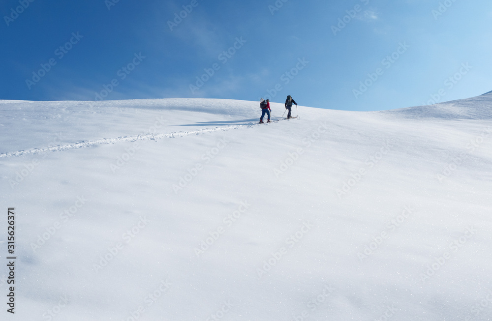 Two men climbing on mountain peak on skis or splitboards at white snow and blue sky background. Ski touring sport activity