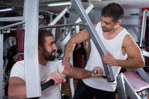 Man helping friend on fitness machine in gym