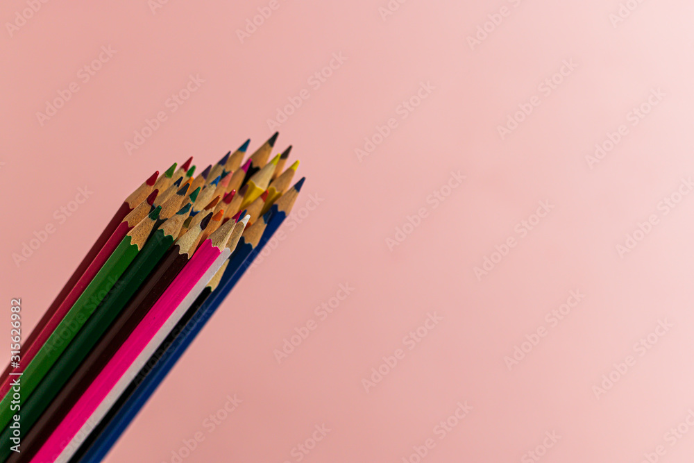 A bunch of multi-colored pencils of different lengths on a pink background in the left corner, tending up. Horizontal close-up