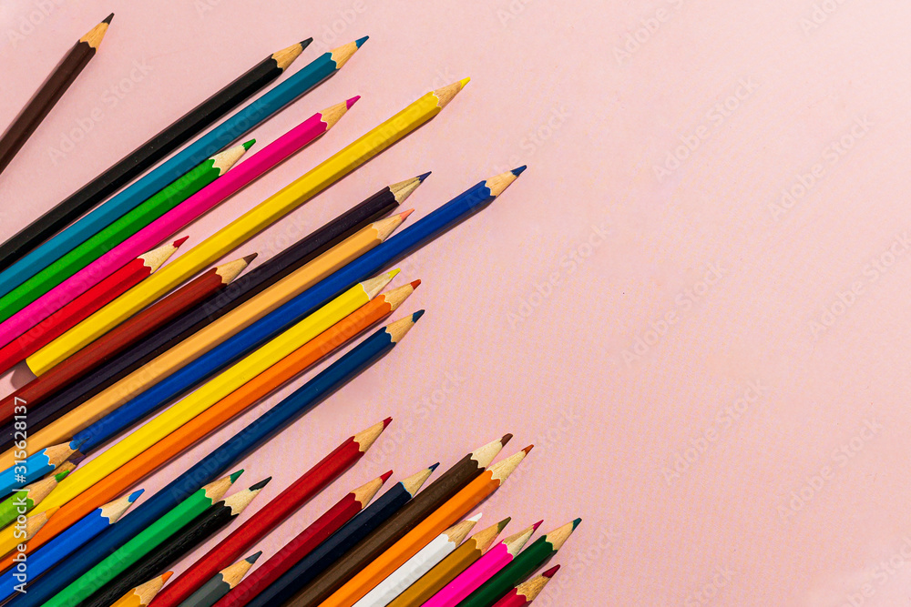 Scattered colored pencils of different lengths on a pink background with a left corner, tending to the center. Horizontal close-up