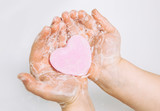 Importance of personal hygiene care. Flat lay view of child washing dirty hands with pink heart shape soap bar, lot of foam. Copy space.