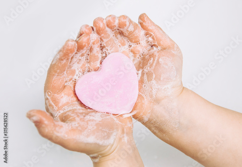 Importance of personal hygiene care. Flat lay view of child washing dirty hands with pink heart shape soap bar, lot of foam. Copy space. photo