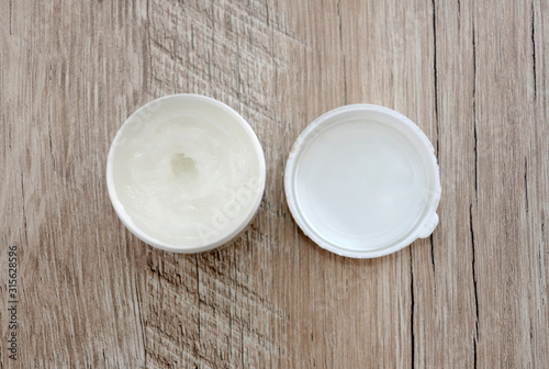 white face cream in a jar on a wooden background. View from above.