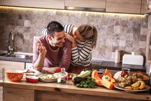 Young couple preparing vegetarian meal.They making fun a the kitchen and preparing vegetables.	