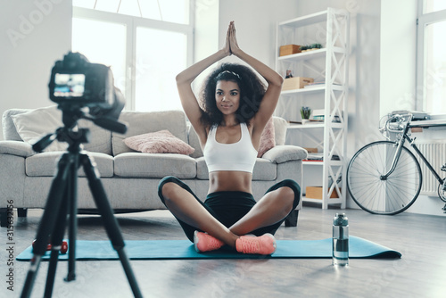 Beautiful young African woman sitting in the yoga while making social media video