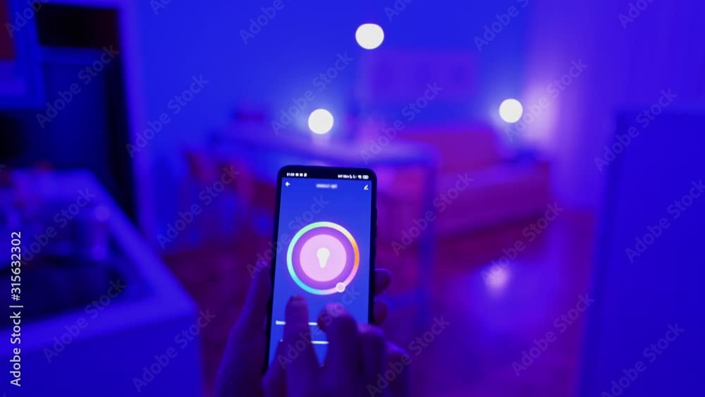 Woman changing color of the lights with smart home app on her smartphone. Smart home house concept. 4K