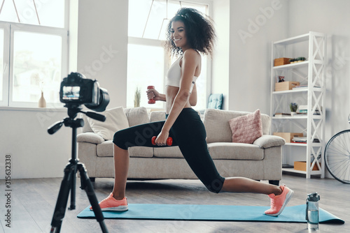 Attractive young African woman exercising using hand weight and smiling while making social media video