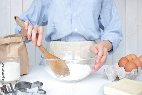 cropped image young woman cooking a cake with recipe, homemade pie in a glass bowl. The ingredients for the cake are laid out on table in a bright kitchen: butter, flour, sugar, eggs, cookie mold