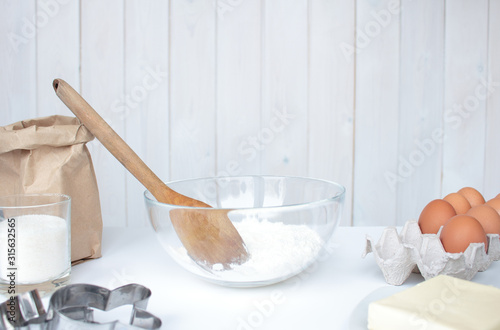 ingredients for home baking are laid out on the table: flour in a glass bowl, butter, sugar, eggs, cookie molds. Preparing to cook a pie in a bright kitchen