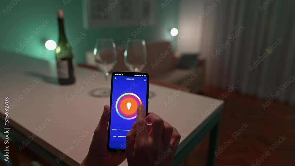 Choosing lighting color for romantic amosphere at home with smart home app. Woman changing color of the lights on her smartphone